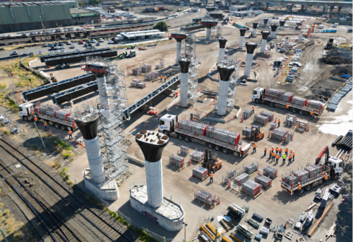 Aerial view of trucks delivering stillaged scaffold to a rail infrastructure site with scaffolded bridge piers