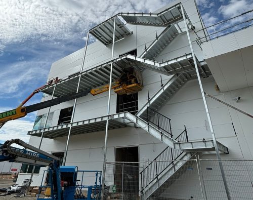 Galvanised steel access stair and platforms being installed on a building facade from a boom lift