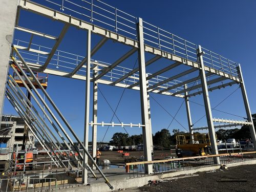 Structural steel portal frame with walkways and handrails being erected on a construction site